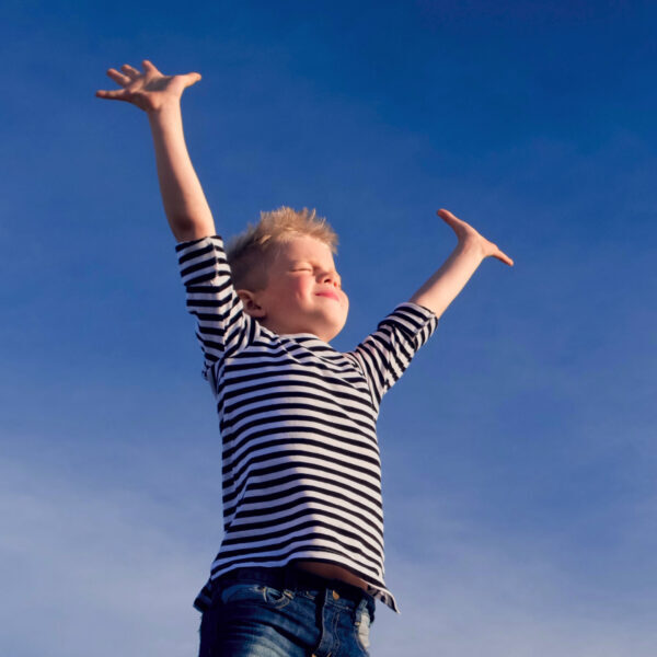Relaxed boy breathing fresh air raising arms over blue sky at summer. Dreaming, freedom and traveling concept.